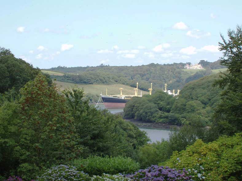 Ausblick von Trelissick Gardens: Ein in der Fal-Mündung parkiertes Hochseeschiff. Im Hintergrund der Sitz der Lords Falmouth